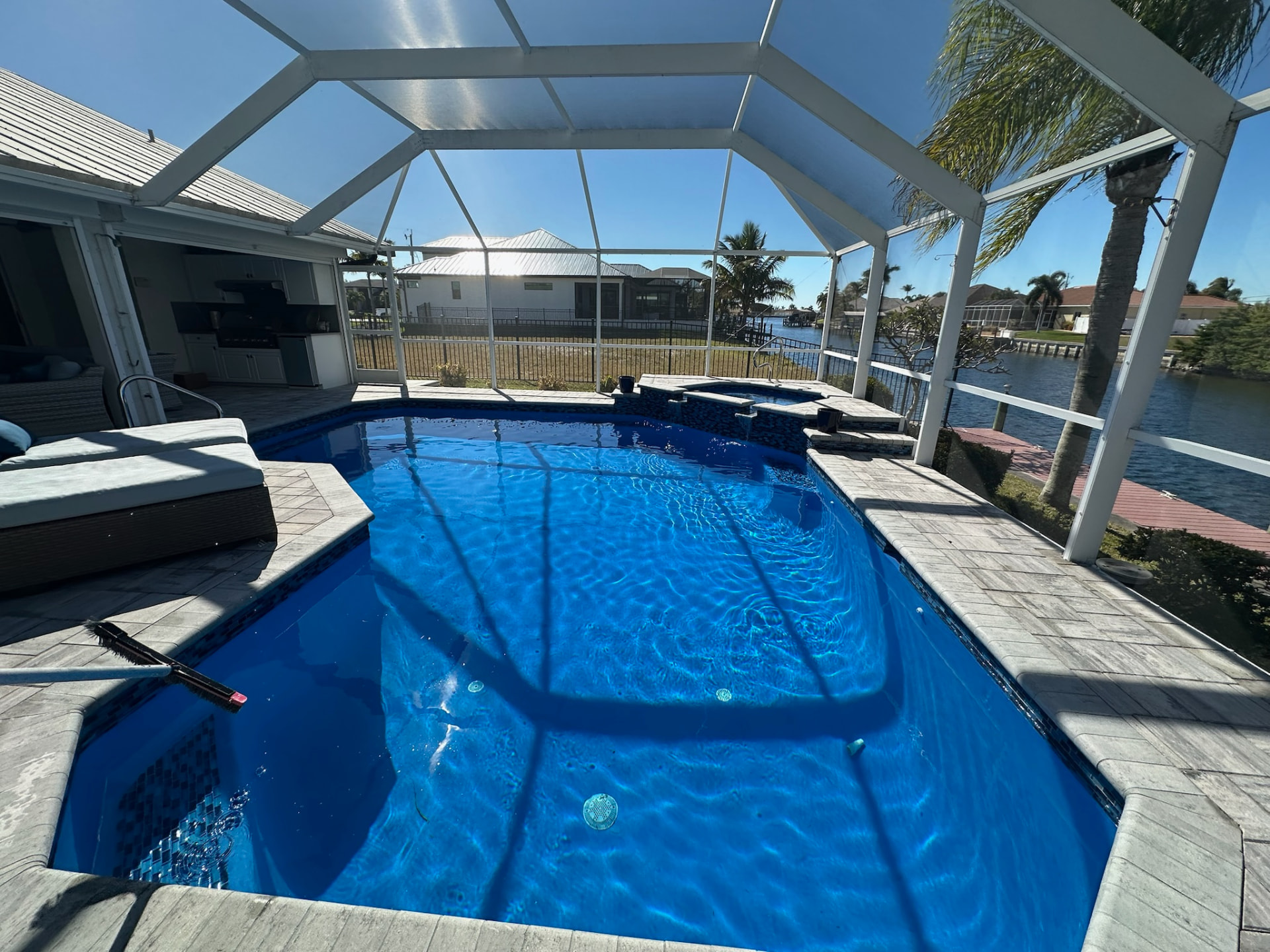 Deep blue resurfaced pool and spa under a white screened lanai